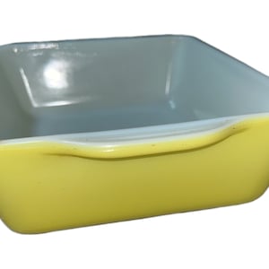 May include: A yellow glass baking dish with a white interior. The dish has a rounded edge and a handle.