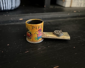 May include: A yellow and black tin toy pipe with a picture of two cartoon characters. The pipe is labeled "PIPE FAVORITE SONG".
