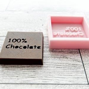 May include: A brown chocolate bar mould with the text "100% Chocolate" and a pink silicone mould with the same text.