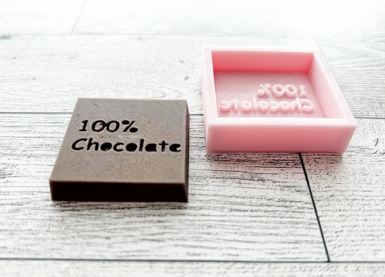 May include: A brown chocolate bar mould with the text "100% Chocolate" and a pink silicone mould with the same text.