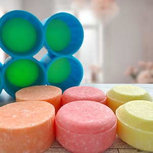 Pu&ograve; includere: Una collezione di shampoo solidi colorati, rotondi e lisci, in arancione, rosa e giallo, accompagnati da un portasapone blu e verde. Il portasapone presenta un design geometrico.