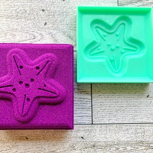 May include: Two square molds, one purple and one green, with a starfish design. The molds are made of a textured material.