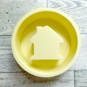 May include: A yellow round container with a raised house-shaped design in the center.