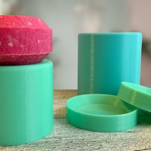 May include: Three 3D printed containers, one stacked on top of the other. The top container is a bright pink, the middle container is a light green, and the bottom container is a light blue.