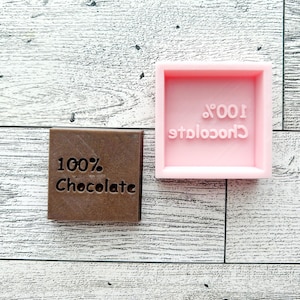 May include: Two chocolate bar moulds, one pink and one brown, both with the text "100% Chocolate" on them.