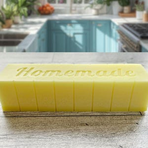May include: A yellow rectangular soap bar with the word "Homemade" carved into the top. The soap is sectioned with vertical lines. The background is a blurred kitchen scene.