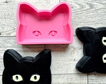 May include: Two black cat-shaped silicone moulds and a pink cat-shaped silicone mould. The moulds have raised eyes and ears.