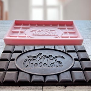 May include: A pink silicone chocolate mold with the words "Love Chocolate" embossed in the center. Next to it is a dark chocolate bar with the same words embossed in the center.