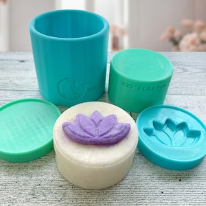 May include: A set of four teal silicone molds for making soap or candles. The molds are round and feature a lotus flower design. One mold is a larger cylinder, and the other three are smaller and have a flat base.