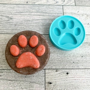May include: A blue silicone mould and a brown soap bar, both shaped like a paw print. The soap is a light pink colour.