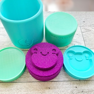May include: A set of five silicone molds for making various shapes. The molds are in different colors, including teal, green, and purple. The molds are shaped like a cylinder, a circle, and two frogs.