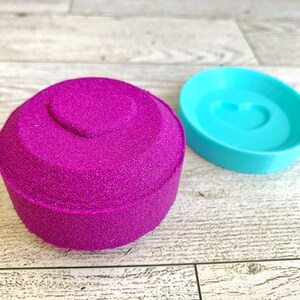 May include: A purple sand mold with a heart-shaped indentation, and a matching blue plastic mold with a heart-shaped indentation.