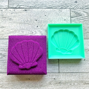 May include: A purple seashell mold and a purple seashell made with the mold. The mold is made of a flexible, clear material. The seashell is made of a textured, sparkly material.