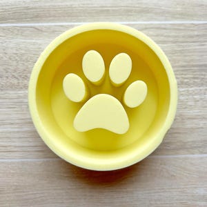 May include: A yellow ceramic dog bowl with a paw print design.