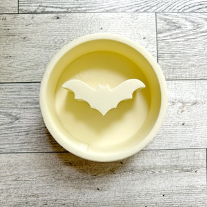 May include: A white ceramic round dish with a raised bat design in the center.