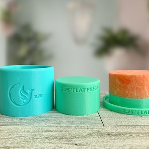 May include: Two turquoise silicone molds for making soap. The larger mold is cylindrical and has a bird logo with the text "2.25" on it. The smaller mold is a flat circle with the text "2.25" FLAT PRESS" on it. A finished soap bar is shown in the smaller mold.