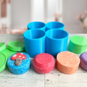 Puede incluir: Cuatro recipientes de plástico azul con tapas, dispuestos en forma de cuadrado. Los recipientes están llenos de barras de jabón de colores, incluyendo rojo, naranja, rosa y morado.