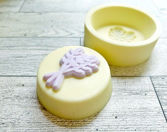 May include: A yellow silicone mold for making soap or candles. The mold is shaped like a circle with a raised design of a lavender sprig in the center. The mold is open and the inside is visible.