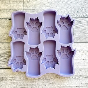 May include: A purple silicone mold with eight paw print shapes. The mold is designed for making small crafts or treats.