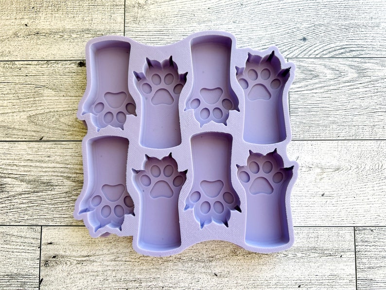 May include: A purple silicone mold with eight paw print shapes. The mold is designed for making small crafts or treats.