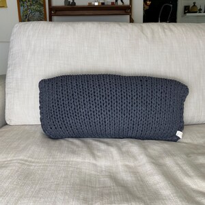 May include: A dark gray knitted throw pillow on a light gray couch.