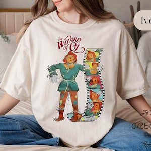 May include: A white t-shirt with a graphic of the Scarecrow from the Wizard of Oz movie. The graphic includes the text "The Wizard of Oz" and a film strip with images of the Scarecrow.