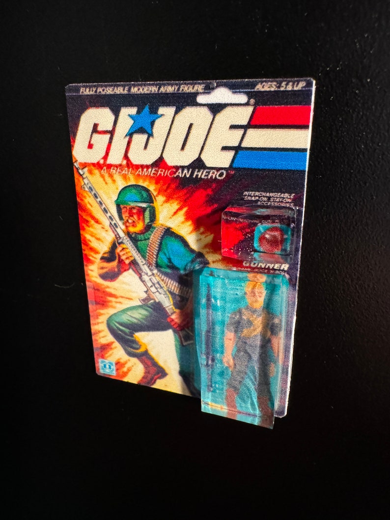 May include: A vintage G.I. Joe action figure on its original card. The card features a soldier illustration with a machine gun against a fiery background. The packaging includes the text "G.I. Joe A Real American Hero" and "Gunner".