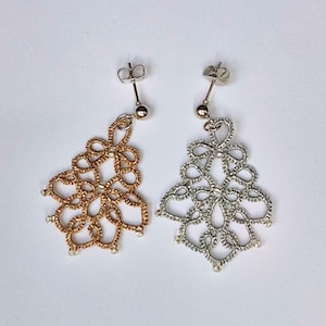 Può includere: Un paio di orecchini pendenti con intricati disegni in pizzo chiacchierino. Un orecchino è color oro metallizzato e l'altro argento metallizzato. Ogni pezzo pende da una semplice chiusura a perno in metallo, mostrando un delicato motivo a cerchi.