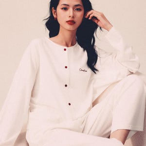 May include: A white long-sleeved pajama top with red buttons and the word "Camelia" embroidered on the chest.