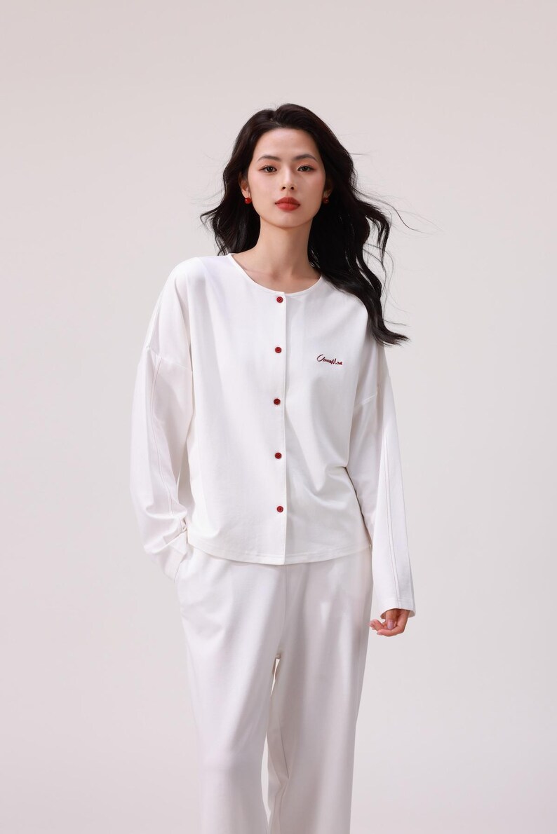 May include: White long-sleeved button-up top and matching pants with red buttons and the word "Commeline" embroidered on the top.