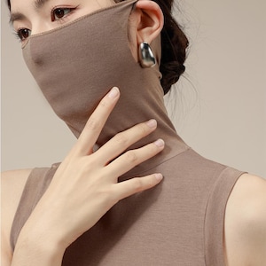 Peut inclure: Un haut sans manches à col roulé marron avec un masque facial marron assorti. Le masque couvre le nez et la bouche et s'étend jusqu'au cou.