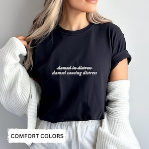 May include: Black t-shirt with white text that reads "damsel-in-distress damsel causing distress".