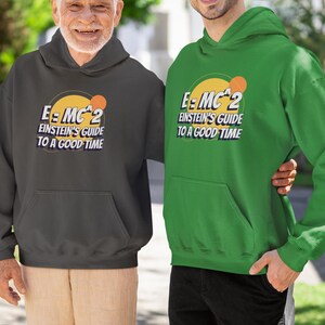Puede incluir: Dos personas con sudaderas con capucha grises y verdes con el texto "E=MC^2 Einstein's Guide to a Good Time" impreso en la parte delantera. El texto está en un círculo amarillo con una pequeña pelota de baloncesto naranja en su interior.