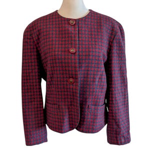 May include: A red and navy houndstooth pattern jacket with three brown buttons and two front pockets. The jacket has a round neckline and is displayed on a mannequin.