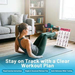 May include: A woman is exercising with a dumbbell while following a workout plan. The workout plan is a white poster with illustrations of exercises. The poster is propped up on a stand. The text on the poster says "Dumbbell Lower Abs Workout". The text at the bottom says "Stay on Track with a Clear Workout Plan".