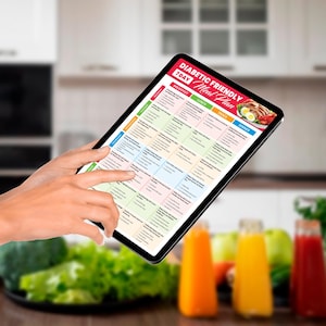 May include: A digital tablet displaying a 7-day diabetic friendly meal plan with breakfast, lunch, snack, and dinner options. The tablet is being held by a person's hand in a kitchen setting.