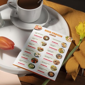 Może przedstawiać: Drukowalne menu z listą opcji lunchowych bogatych w białko. Menu zawiera takie dania jak kanapka z sałatką jajeczną, sałatka z makaronem i kurczakiem oraz sałatka z makaronem, łososiem i krewetkami. Menu znajduje się na białym talerzu z filiżanką kawy i ż&oacute;łtym kwiatem.