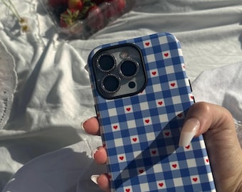 May include: A blue and white checkered phone case with red hearts. The case has a black camera lens cover with four small circles.