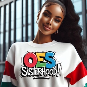 Puede incluir: Una sudadera blanca con mangas de color rojo, verde y azul. La parte delantera de la sudadera tiene un gráfico colorido que dice "OES Sisterhood!"