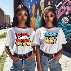 May include: Two women wearing white t-shirts with colorful graphic text. The text on the left shirt says "The Devil is a Liar... Yeah Yeah! Yeah Yeah!" The text on the right shirt says "Victory is Mine Yeah!"