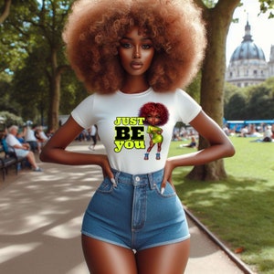 May include: A white t-shirt featuring a cartoon illustration of a woman with red hair and a yellow dress. The text "JUST BE YOU" is printed in yellow on the shirt.