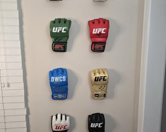May include: Collection of eight miniature UFC boxing gloves in various colors, including blue, silver, green, red, gold, white, and black. Each glove features the UFC logo and other details. They are mounted on a wall.