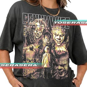 Puede incluir: Camiseta gris oscuro con un diseño de Pennywise el payaso de la película "IT." El diseño incluye múltiples imágenes de la cara del payaso y el texto "Pennywise." La camiseta tiene un aspecto vintage y desgastado.