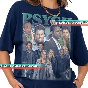 May include: A dark navy blue short-sleeve t-shirt featuring a large graphic print of the television show Psych. The design includes a collage of the cast members, the word PSYCH in large letters at the top, and lightning bolt accents.