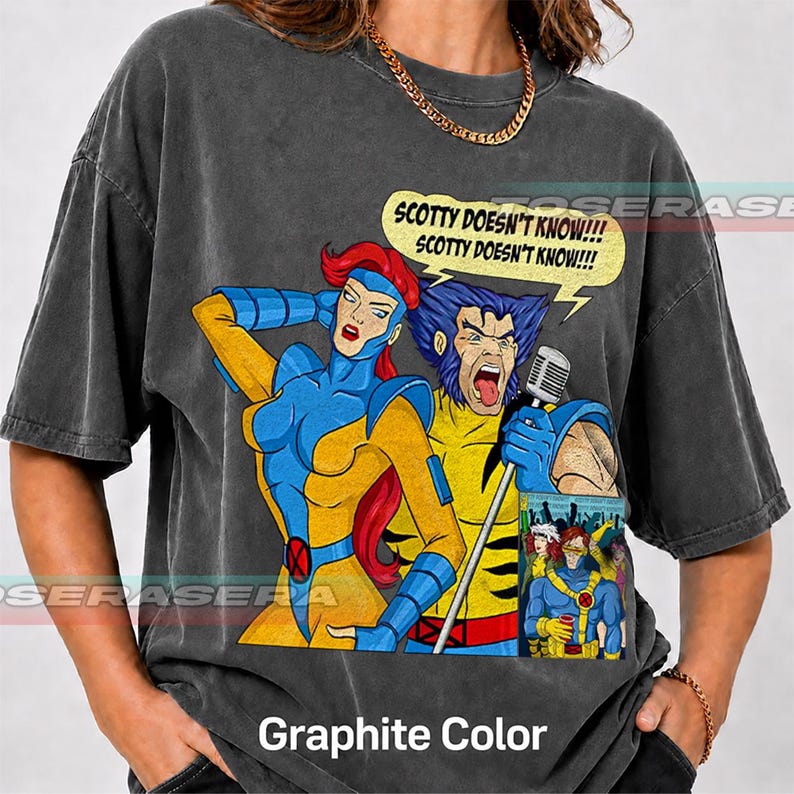 May include: A charcoal gray t-shirt featuring a graphic print of two comic book characters. One character has red hair and a blue and yellow suit, while the other has blue hair and a yellow and blue suit, holding a microphone with the text SCOTTY DOESN'T KNOW!!!