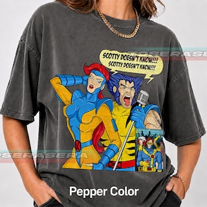 May include: A charcoal gray short-sleeve t-shirt featuring a graphic of Jean Grey and Wolverine from X-Men. Wolverine holds a microphone and a speech bubble reads, "SCOTTY DOESN'T KNOW!!! SCOTTY DOESN'T KNOW!!!" A smaller inset image shows Cyclops.
