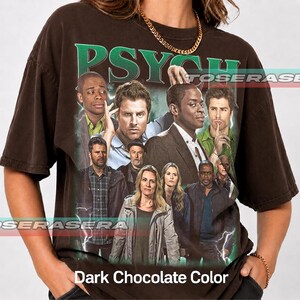 May include: A dark chocolate brown short-sleeve t-shirt featuring a large graphic print of the Psych television show cast. The word PSYCH is printed in large green letters at the top. The design includes multiple characters and lightning effects.