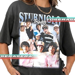 May include: Dark gray t-shirt featuring a graphic of a group of young men with the text "STURNIOLO Triplets" in a stylized font. The graphic includes images of the young men wearing hats and smiling. The shirt has a vintage, worn look.