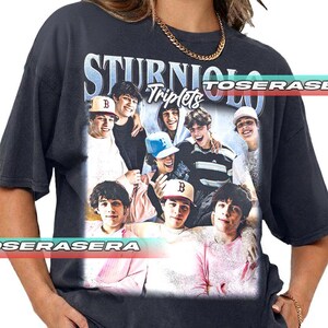 May include: Dark gray t-shirt featuring a graphic of several young men with the text "STURNIOLO Triplets" in a vintage style. The image includes a variety of colors and the t-shirt has a classic crew neck design.