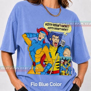 May include: A periwinkle blue t-shirt featuring a graphic print of two comic book characters, one with red hair and one with blue hair, singing into a microphone. A yellow speech bubble above them contains the text SCOTTY DOESN'T KNOW!!!
